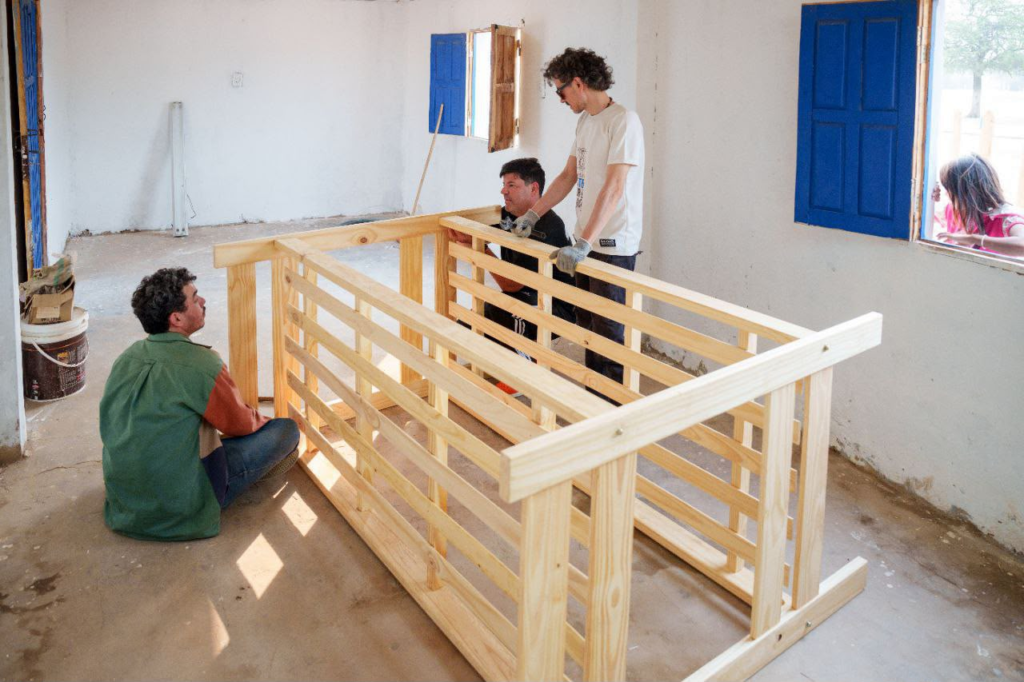 Voluntarios armando camas cuchetas de madera dentro del albergue estudiantil de Tres Pozos, parte del equipamiento aportado por Rotary Club Resistencia